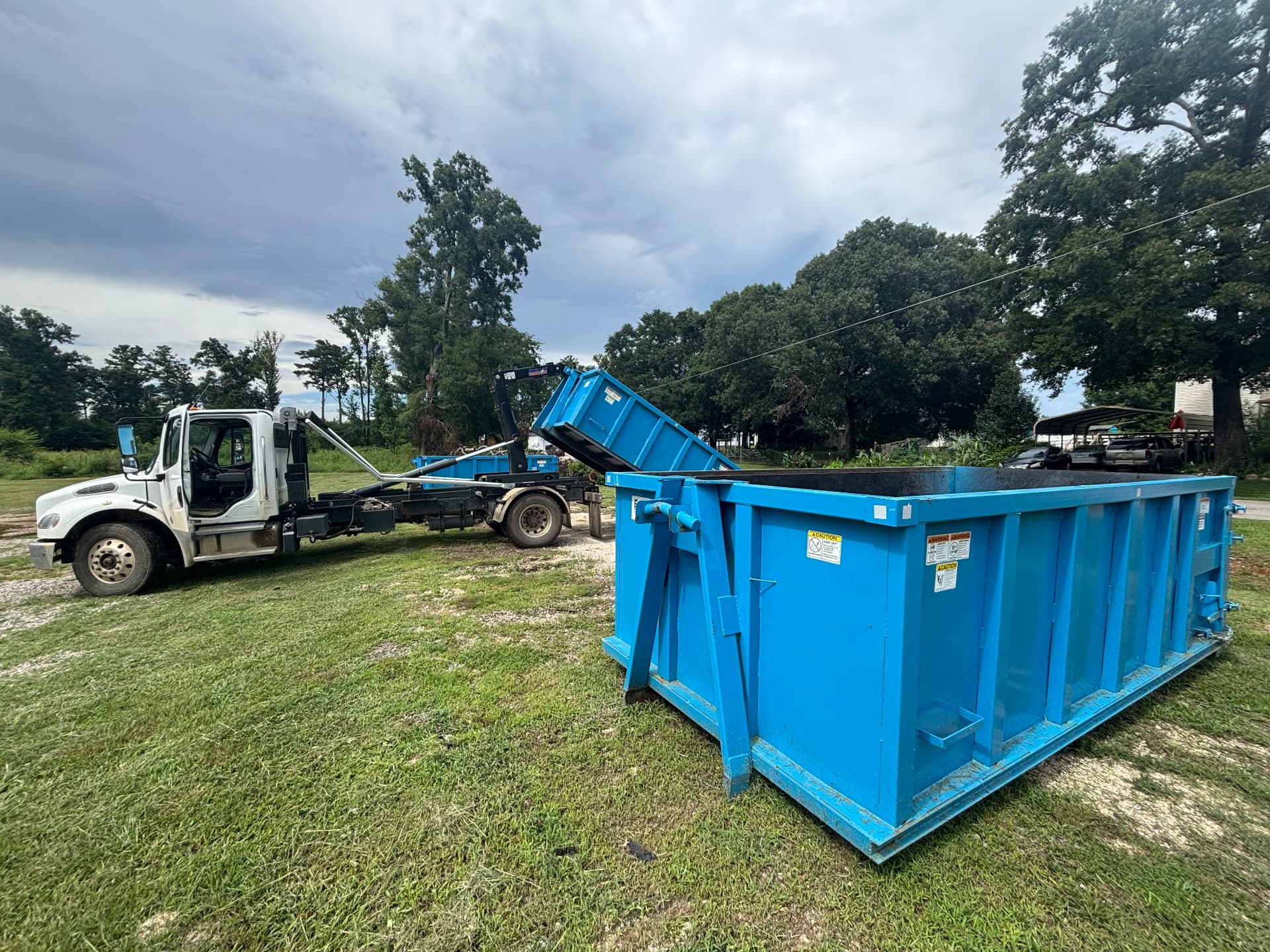 Riba Roll-Off hooklift truck delivering a 20 yard dumpster onto a grass lot