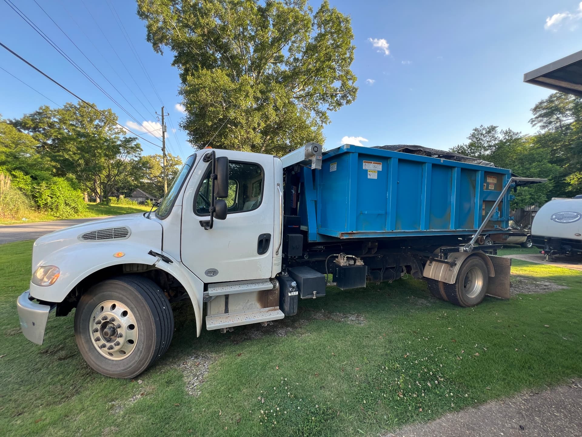 White hooklift roll off truck loaded with a blue dumpster ready for delivery