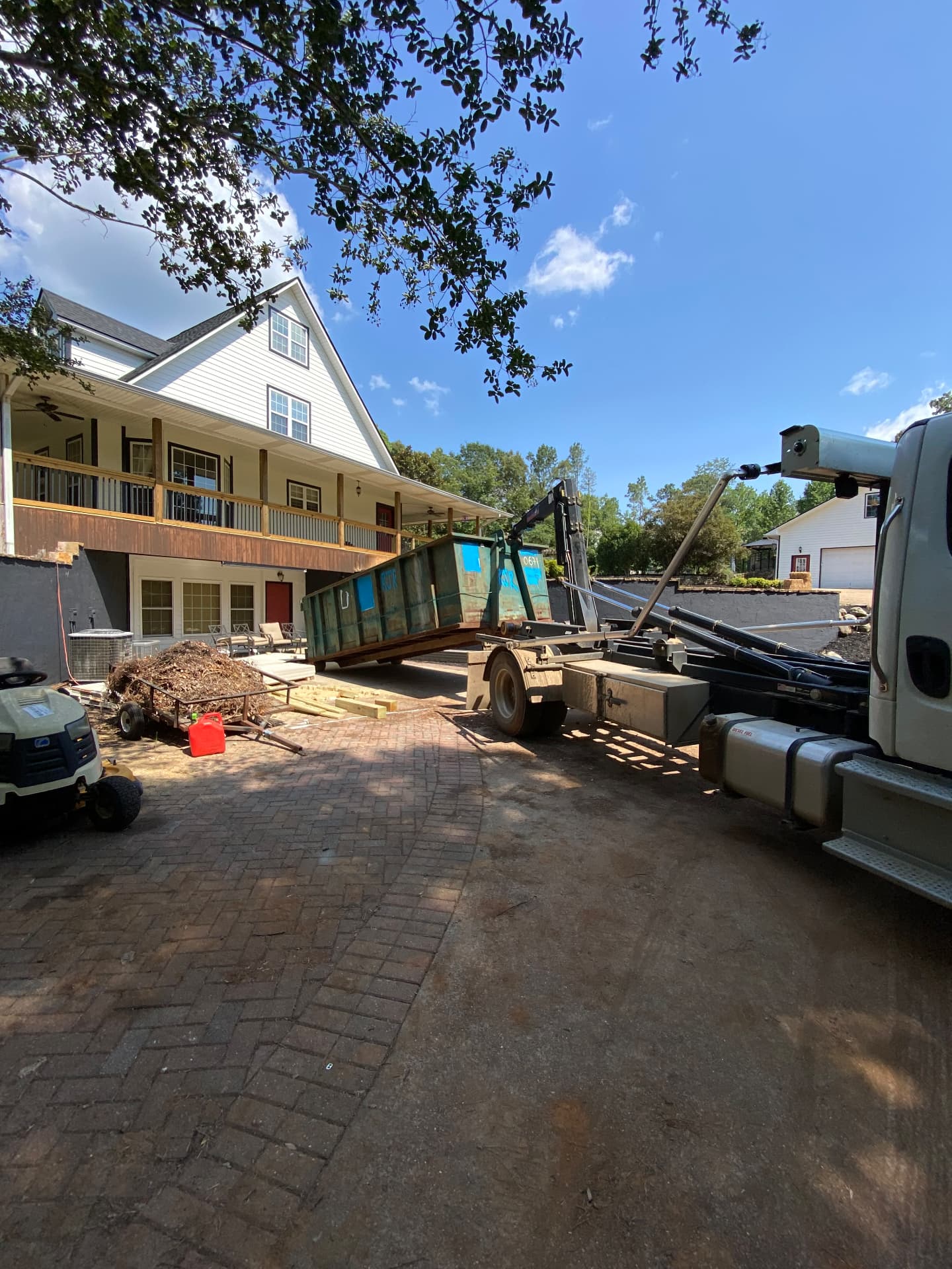 Hooklift truck placing a roll off dumpster on a paver driveway for a remodel