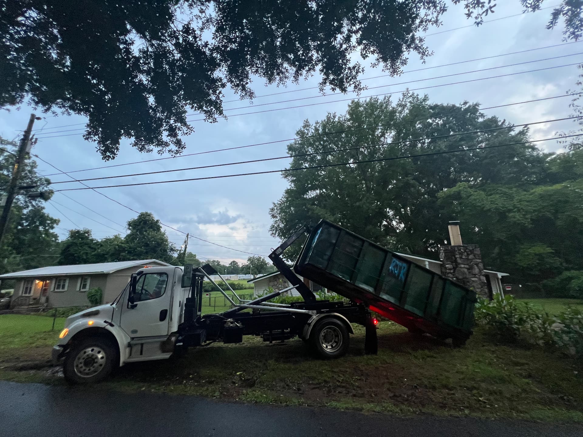 Hooklift truck setting a dumpster down gently beside a home